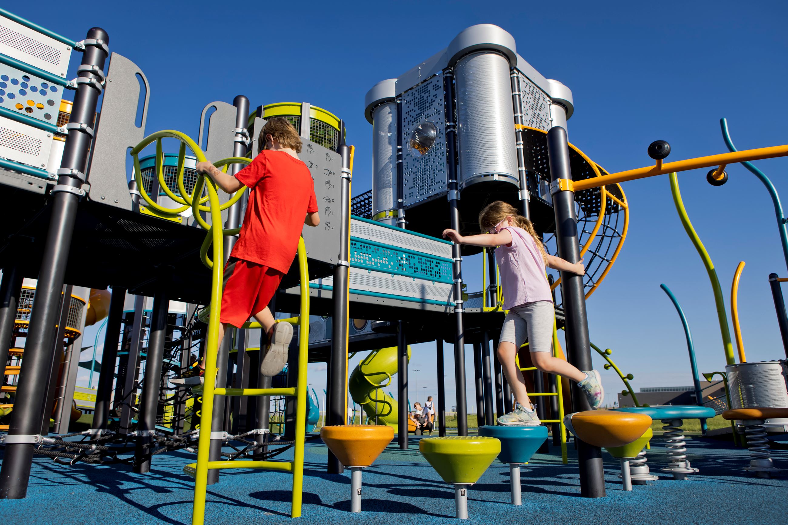 Boy climbs a ladder on the play structure while a girl leaps from one stepping stone to the next